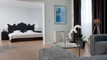 A modern hotel room with a bed, a glass table with a bottle and glasses, a potted orchid, a lamp, and a grey armchair.