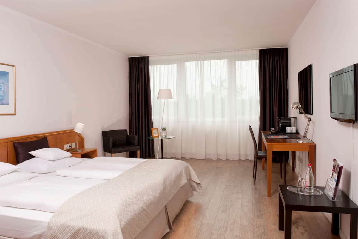 A hotel room with a large bed, a desk, a chair, a television, and a window with curtains.
