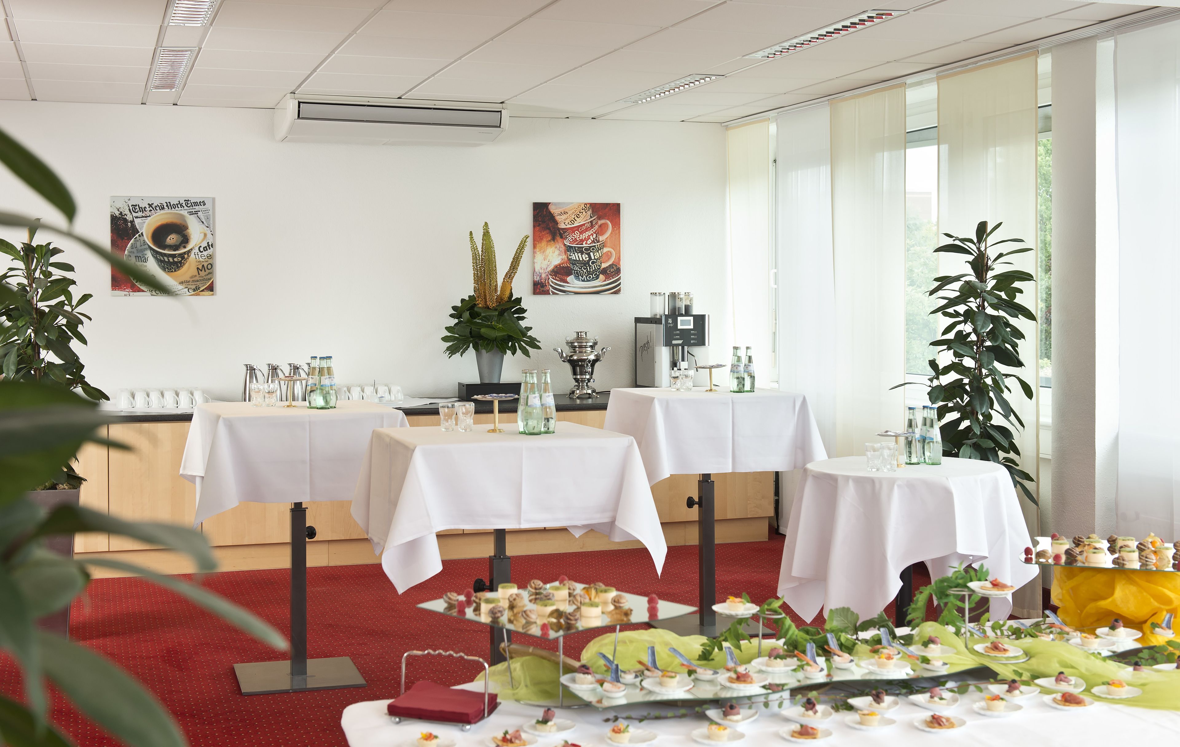 Un salón de conferencias con mesas dispuestas para una reunión, con manteles blancos, cristalería y diferentes tipos de comida.