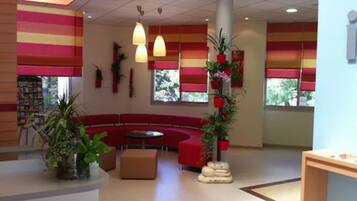 Un hall d’entrée moderne avec un espace détente aux fauteuils rouges, un comptoir d’accueil en bois et des plantes en pot.