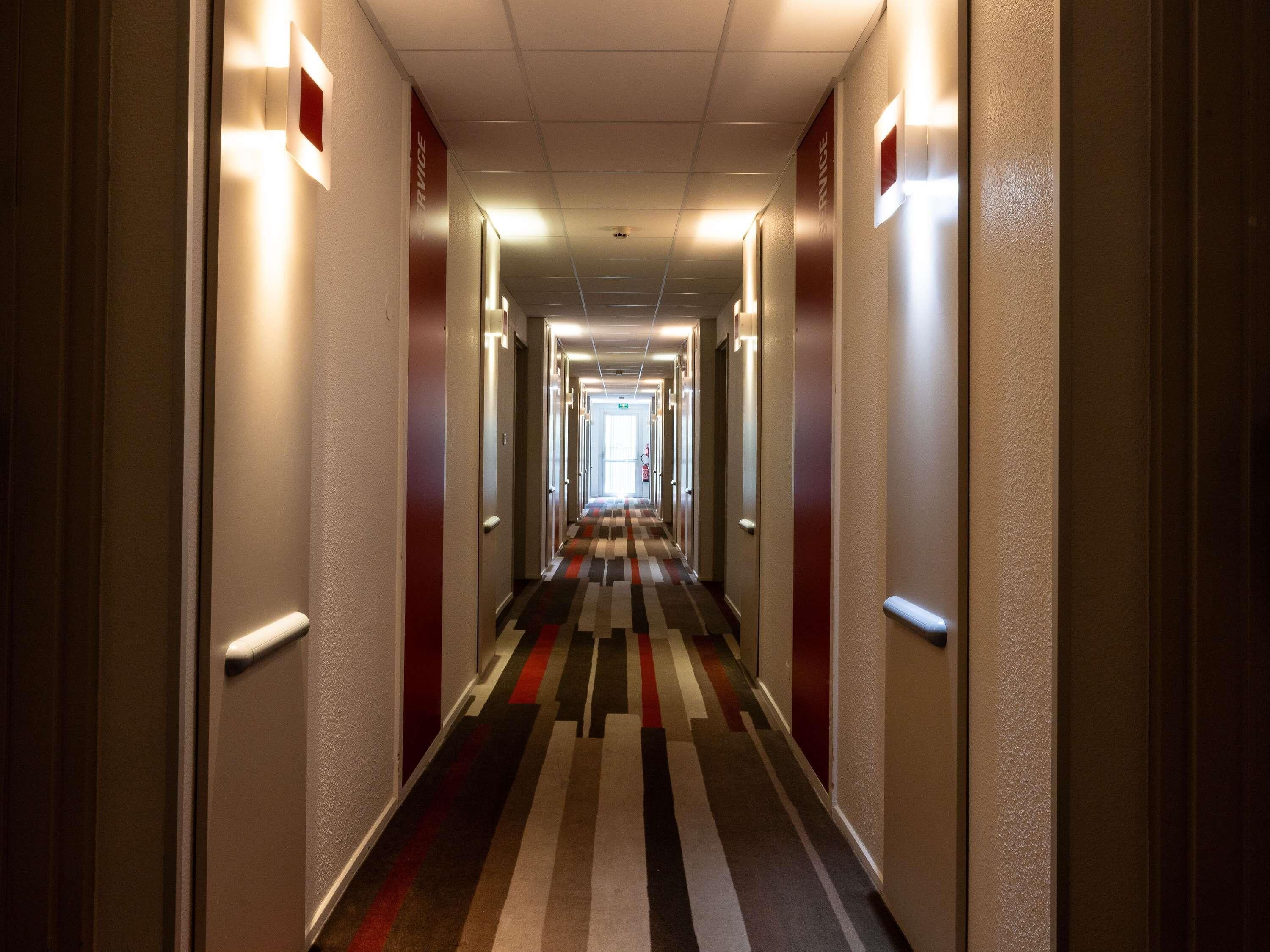 A hotel hallway with a striped carpet, doors on both sides, and a ceiling light.