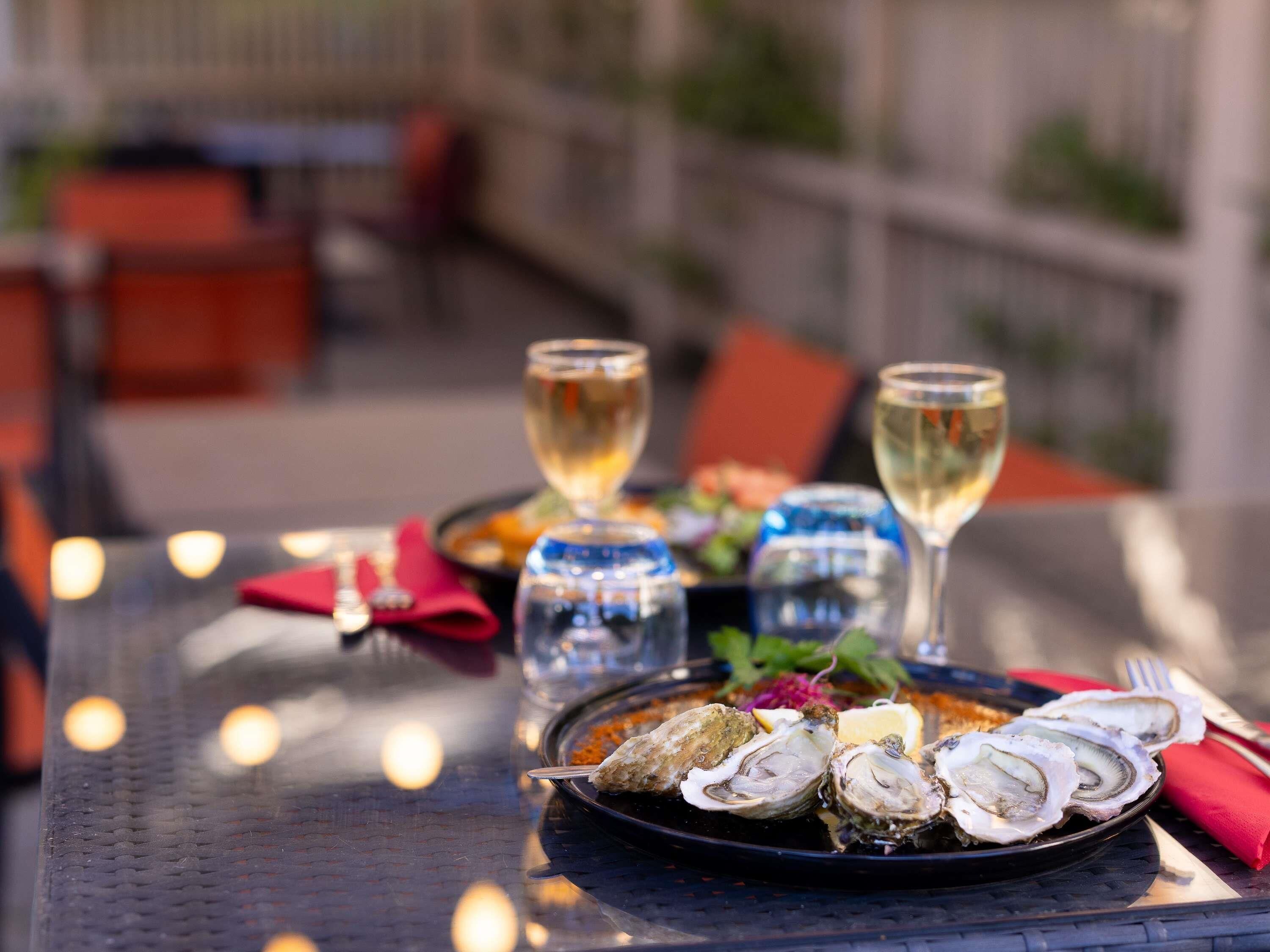 Une table à manger avec une assiette d’huîtres, deux verres de vin blanc et une serviette rouge.