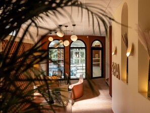A modern interior with a curved reception desk, pendant lighting, and a view through a large arched window. - ibis Sète Balaruc les Bains Bien-être et Spa Hotel (Balaruc-les-Bains)