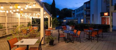 An outdoor patio area with tables and chairs, string lights, and potted plants.