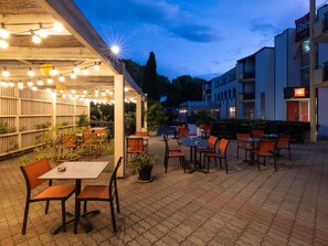 Un'area patio all'aperto con tavoli e sedie, luci a stringa e piante in vaso.