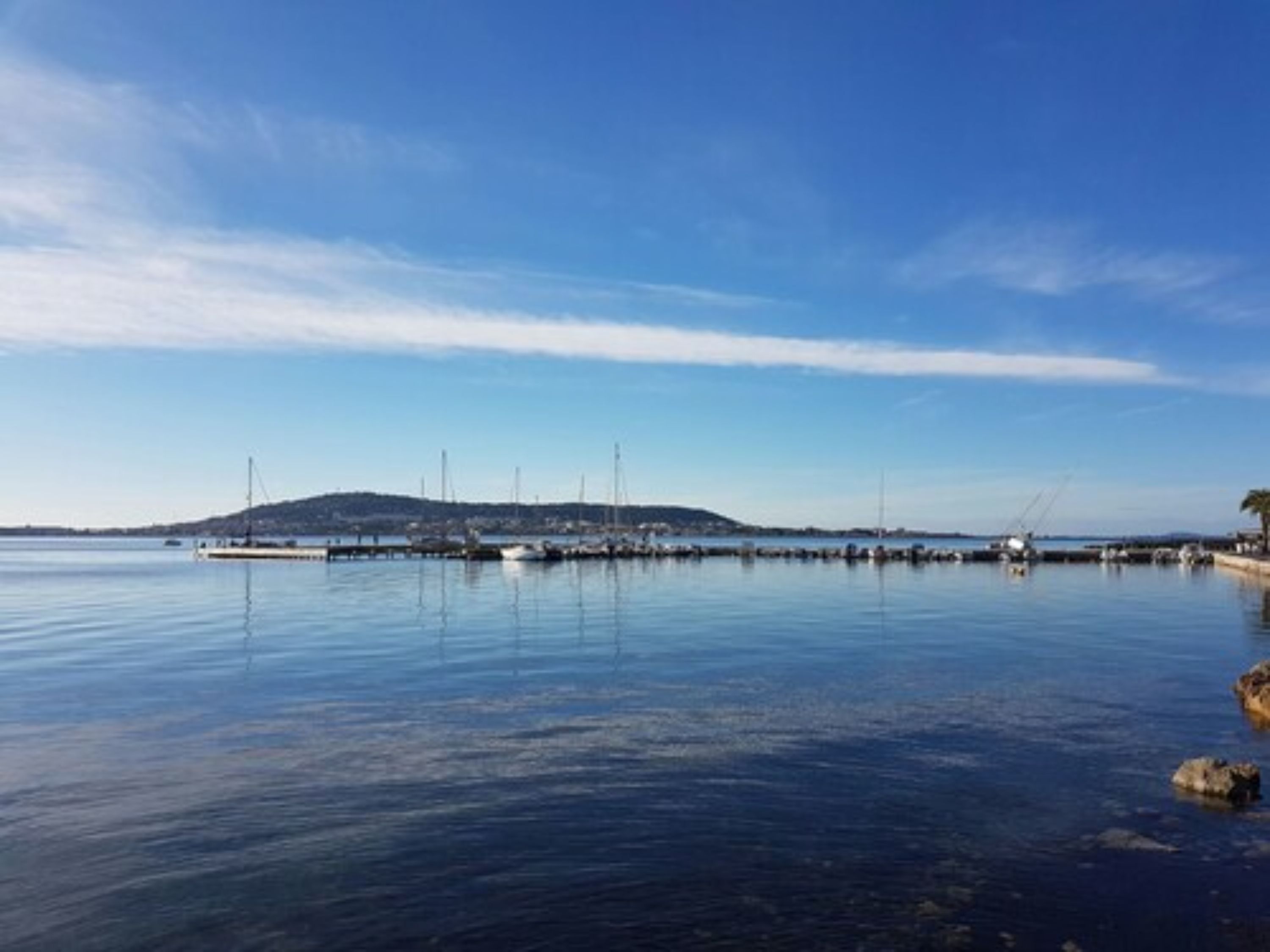 Una orilla tranquila con barcos amarrados en el muelle, cielo despejado y una colina distante.