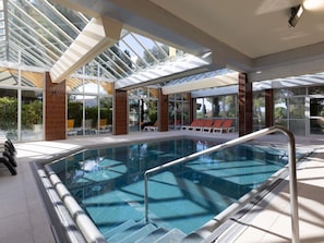 An indoor swimming pool with clear glass walls, a sunlit area with lounge chairs, and a view of greenery outside. - ibis Sète Balaruc les Bains Bien-être et Spa Hotel (Balaruc-les-Bains)