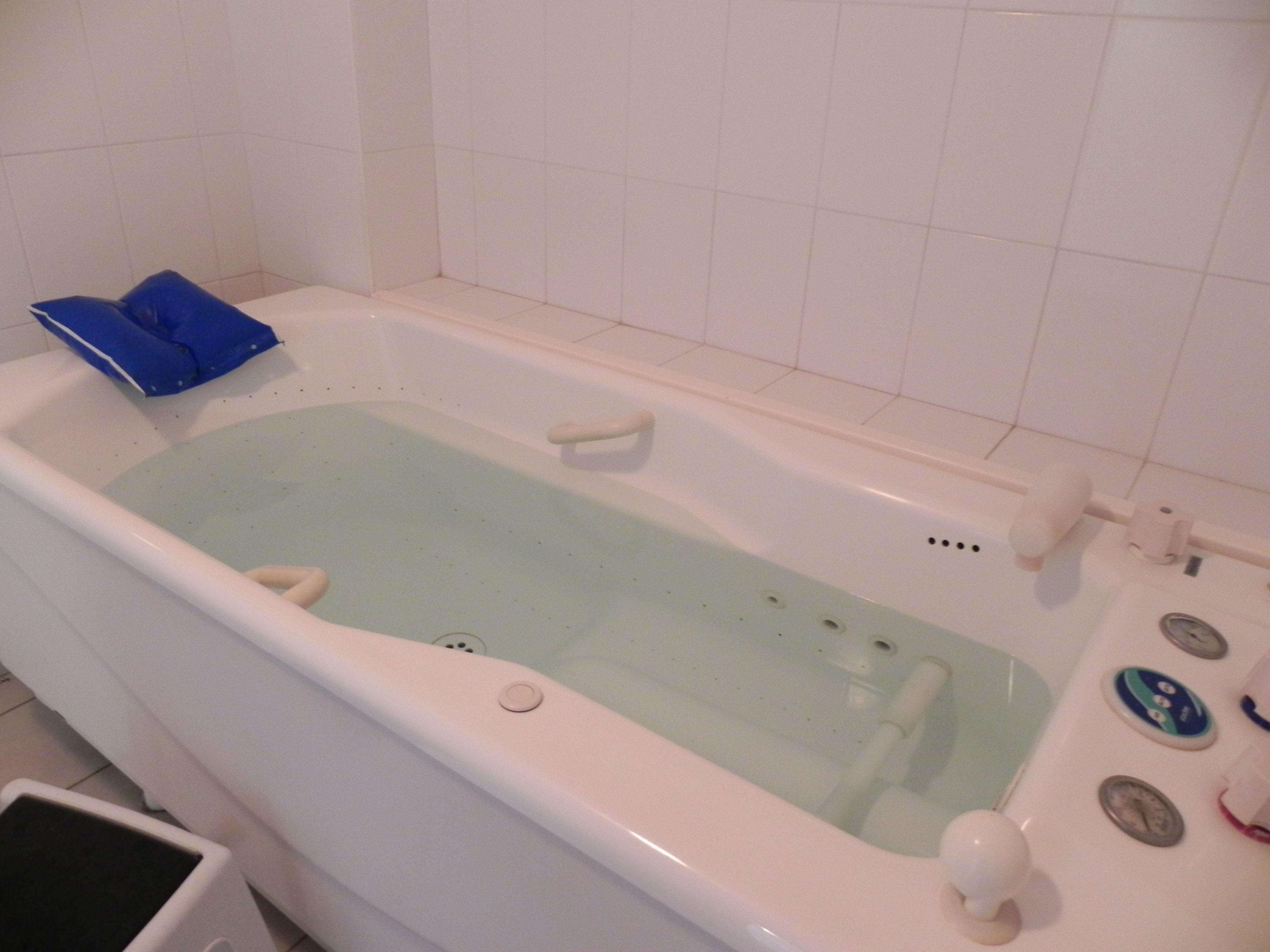 Una bañera con un felpudo azul para baño, una cortina de ducha blanca y una pared de azulejos blancos.
