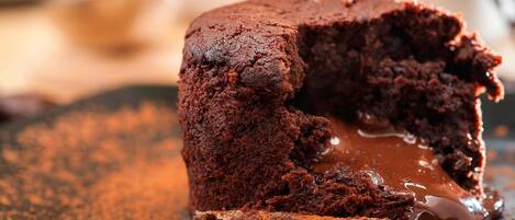 A chocolate lava cake with a gooey center, dusted with cocoa powder, on a dark plate.