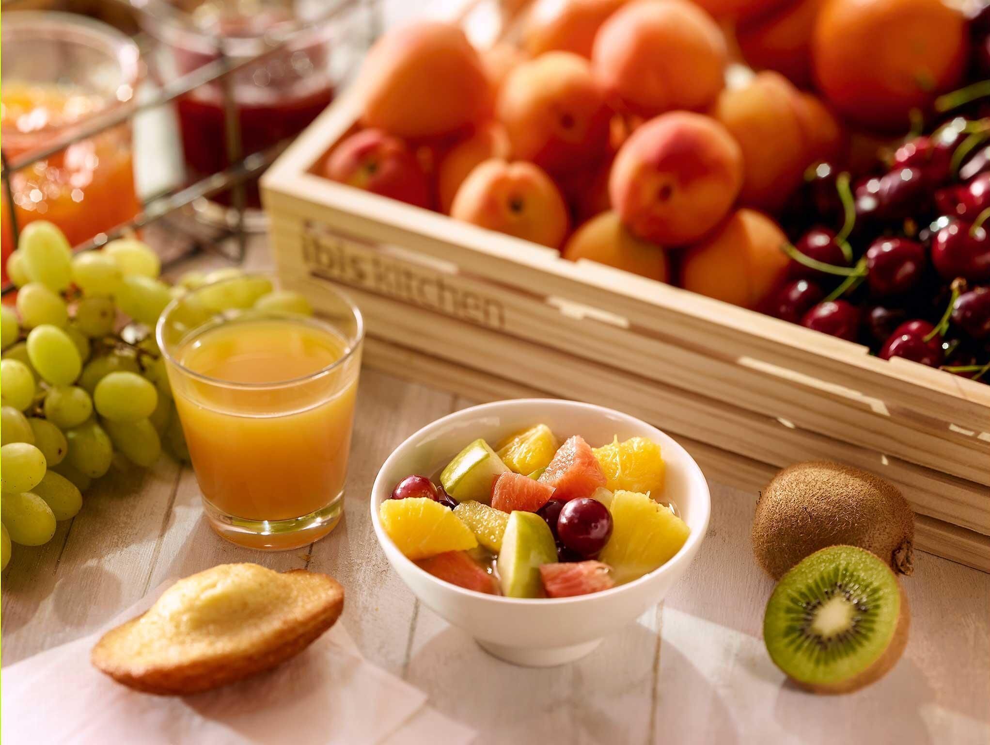 A fruit bowl with various fruits, a glass of orange juice, and a crate of peaches.