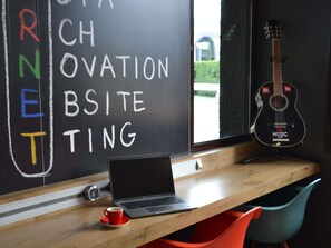 A laptop on a wooden desk with a chalkboard behind it, a guitar, and a cup of coffee. - ibis Chambery (Chambery)