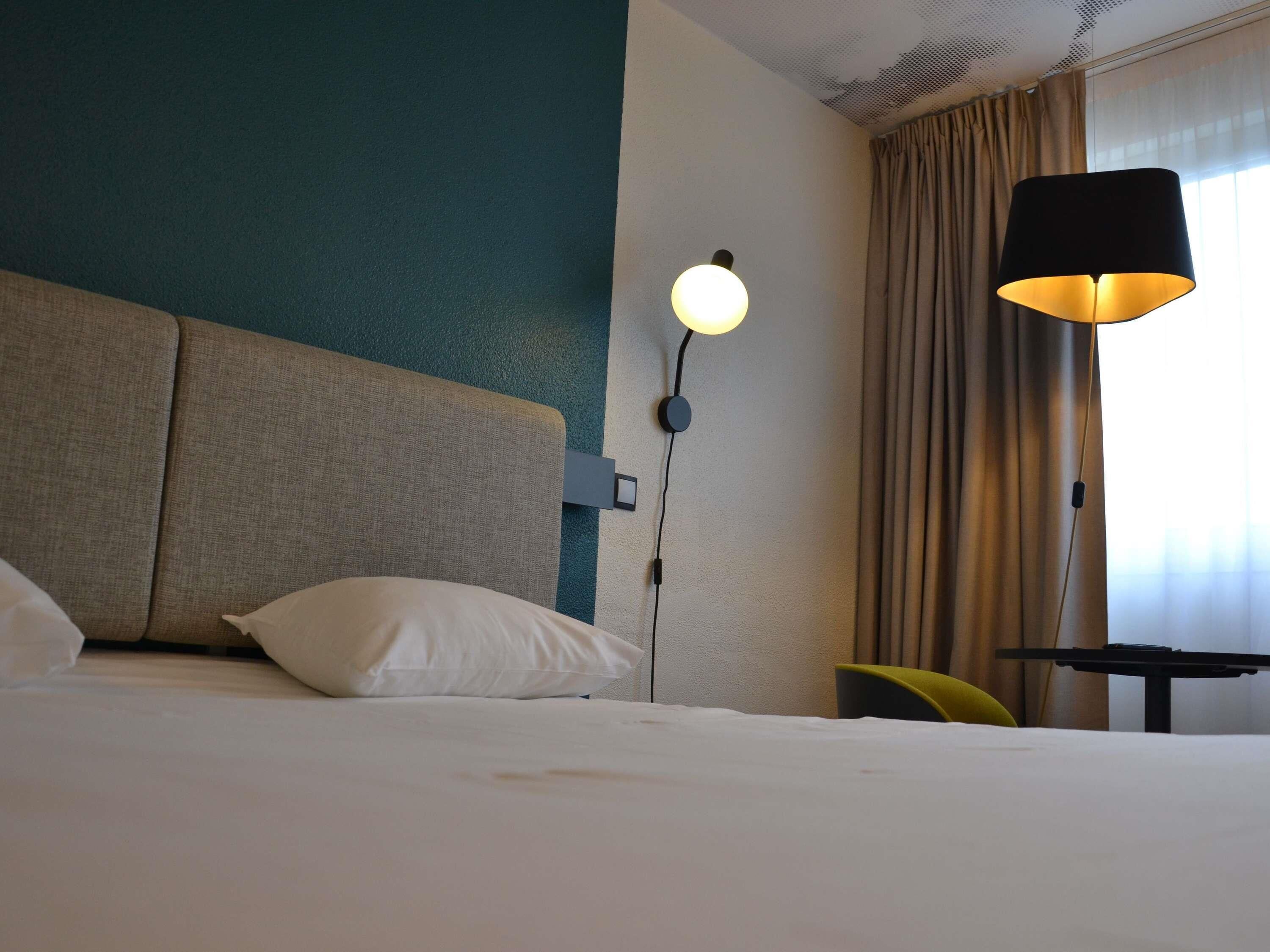 Una habitación de hotel con cama, lámpara de pared, una mesa y una silla.