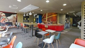 Una cafetería moderna con sillas y mesas coloridas, y una barra central.