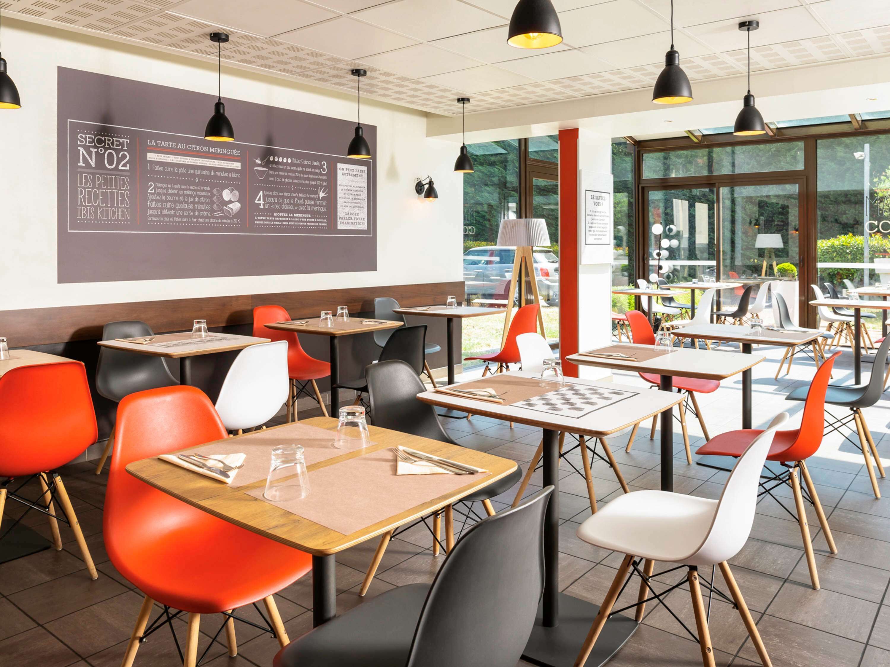 A modern cafe interior with tables and chairs, a menu board, and large windows offering a view of the outdoors.