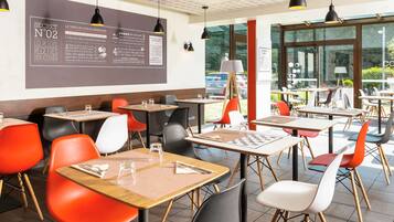 A modern cafe interior with tables and chairs, a menu board, and large windows offering a view of the outdoors.