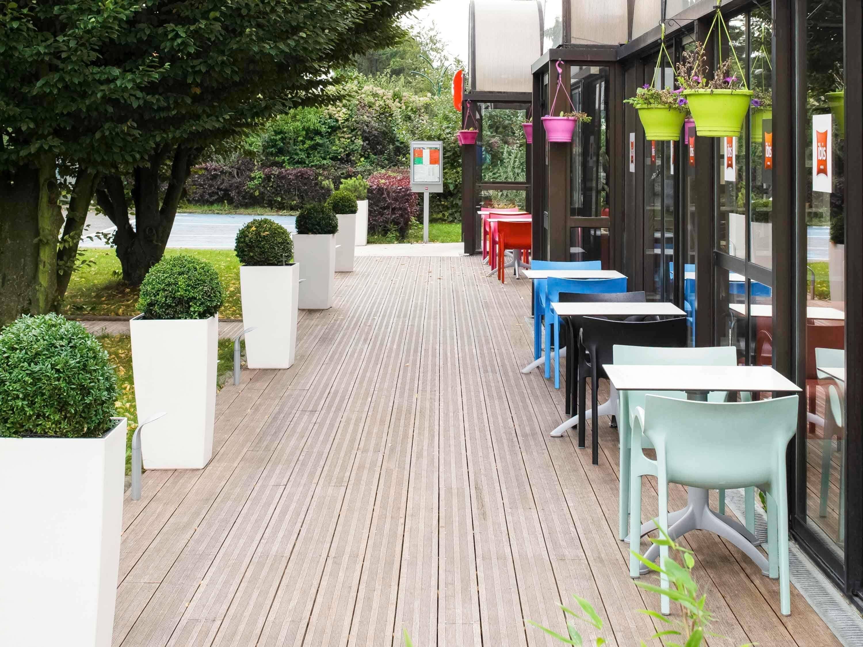 An outdoor seating area with tables and chairs, potted plants, and a view of the street.