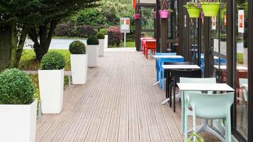 An outdoor seating area with tables and chairs, potted plants, and a view of the street.