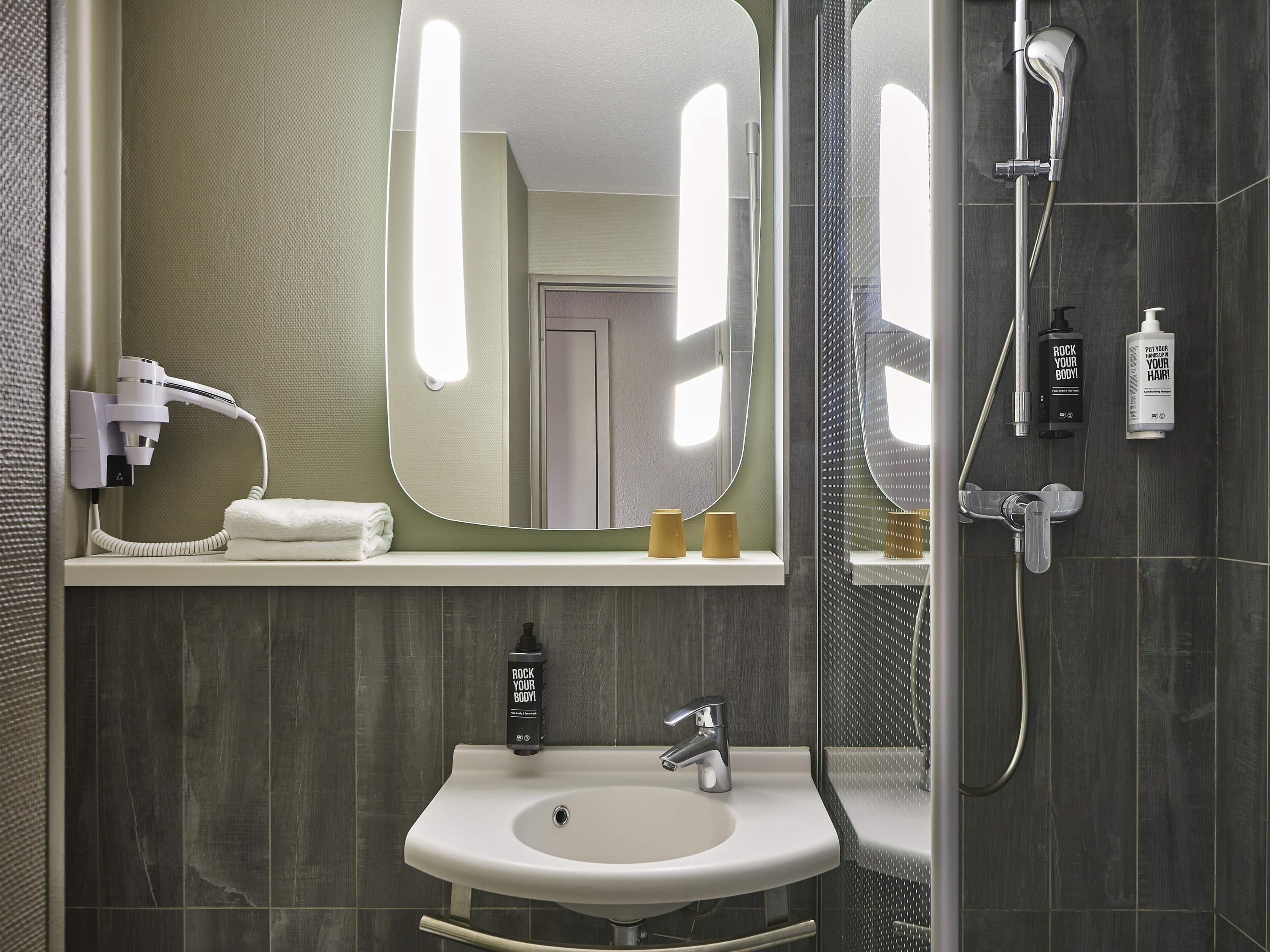 A bathroom with a sink, mirror, hairdryer, and shower.. ibis Marne La Vallee Emerainville