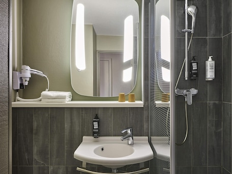 A bathroom with a sink, mirror, hairdryer, and shower.. ibis Marne La Vallee Emerainville