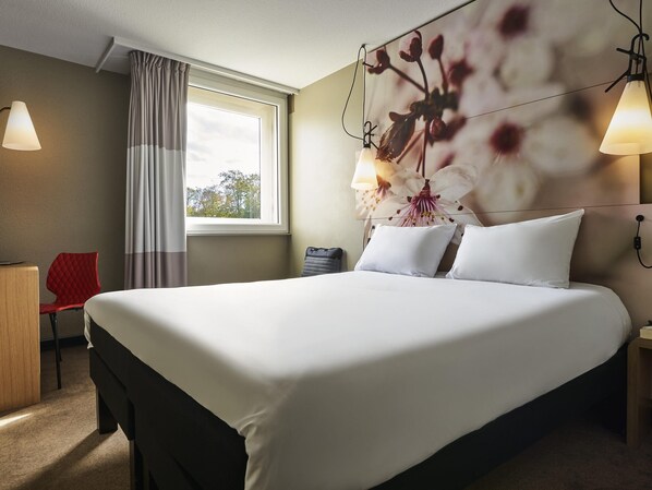 Une chambre d’hôtel avec un grand lit, un bureau, une chaise, une fenêtre avec des rideaux et des lampes fixées au mur.