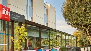 Un espace extérieur aménagé avec des tables et des chaises, une façade en verre et une enseigne indiquant « Marne La Vallée Emerainville ».