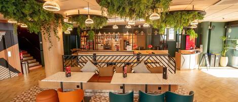 A modern interior with a bar area, seating with a patterned rug, and hanging greenery.