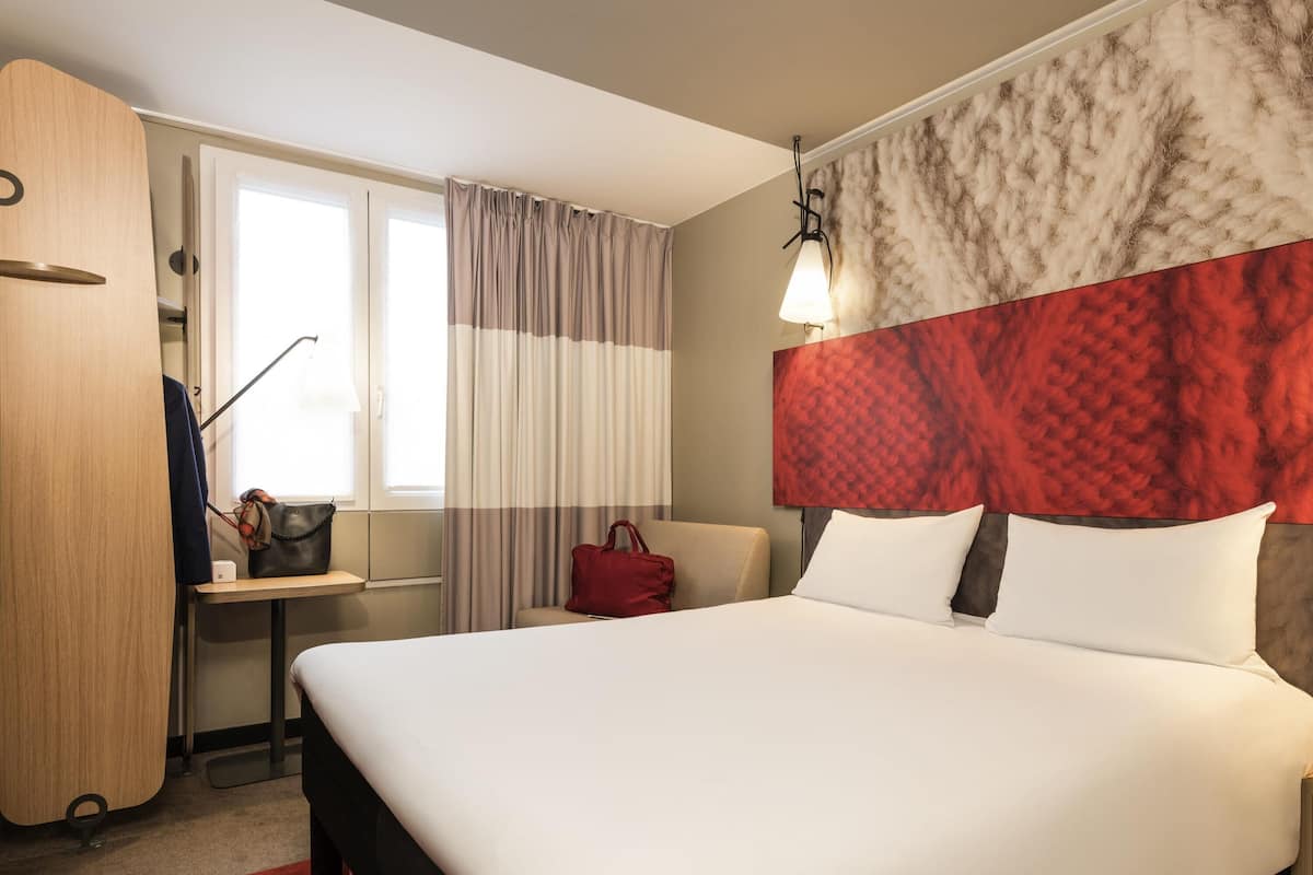 Ein Hotelzimmer mit Bett, Schreibtisch, Stuhl, Kleiderschrank und einem Fenster mit Vorhängen.