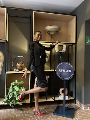 A person in a black suit and red heels standing in a room with a sign labeled 'WOJO' and a plant on a shelf. - ibis Styles Abidjan Plateau (Abidjan)