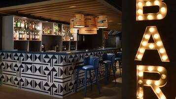 A bar area with a patterned counter, blue bar stools, and illuminated letters spelling 'BAR'.
