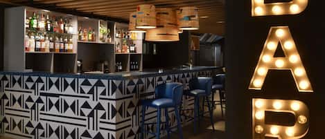 A bar area with a patterned counter, blue bar stools, and illuminated letters spelling 'BAR'.