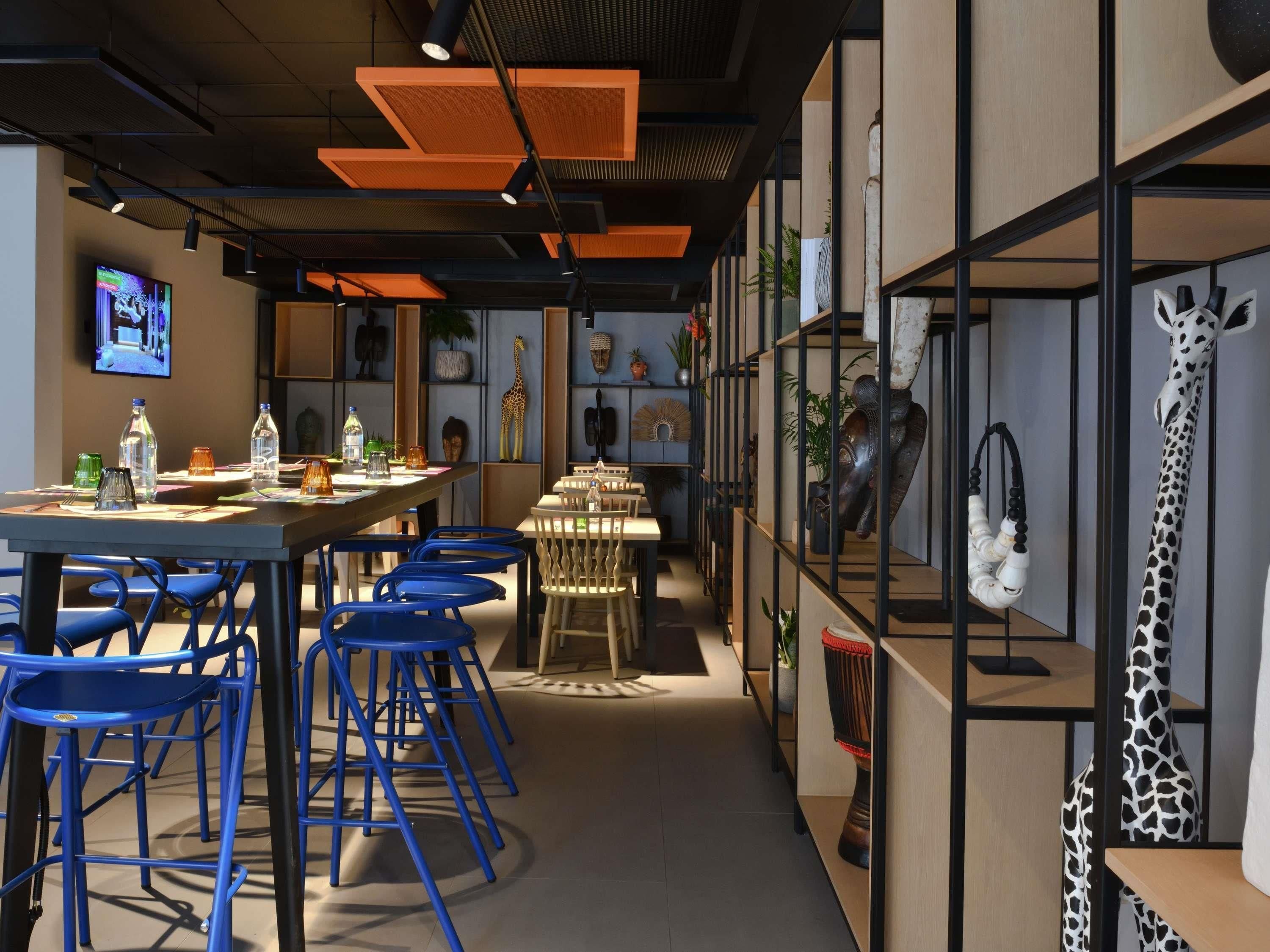 Un comedor moderno con mesas altas, sillas azules y varios objetos decorativos, incluyendo una escultura de jirafa.