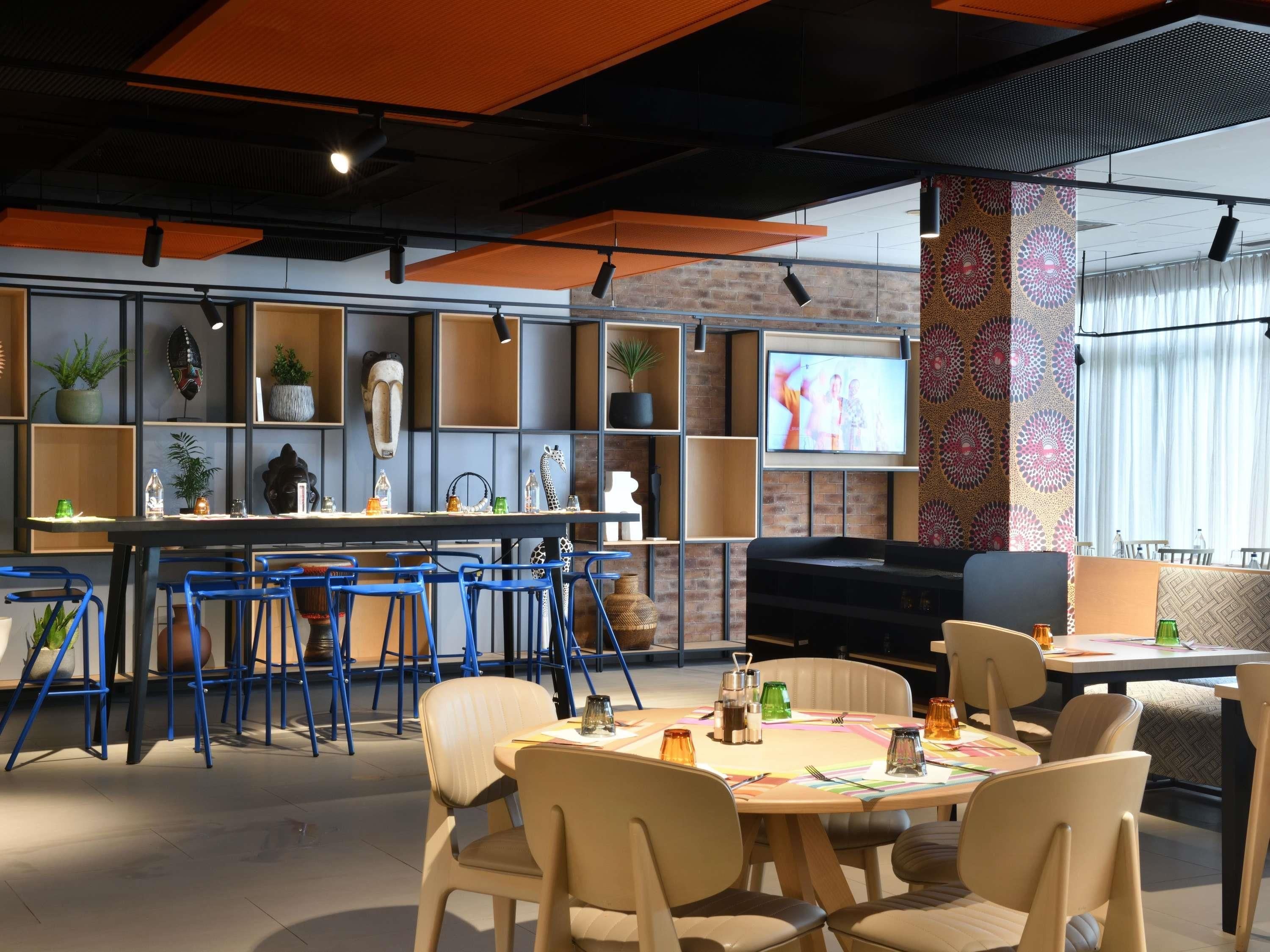 Un comedor moderno con una mezcla de sillas azules y beige, una mesa central con un mantel individual colorido y un televisor montado en la pared.