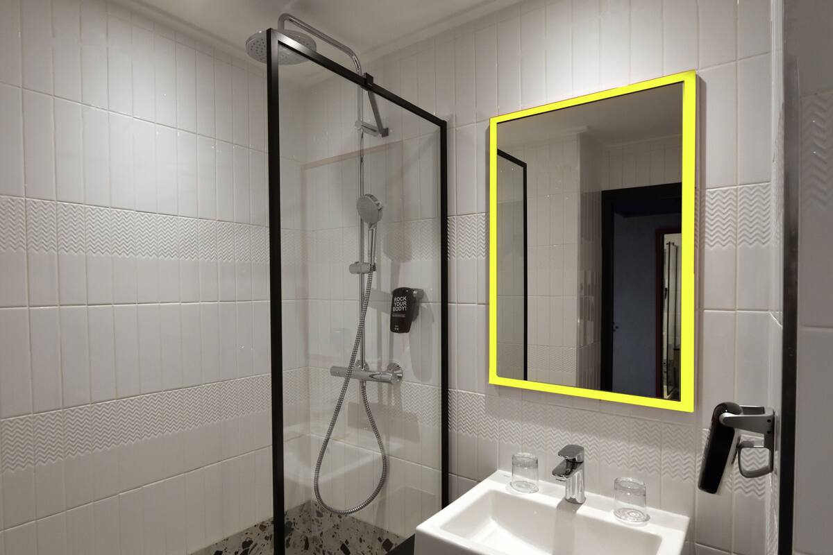 A bathroom with a glass-enclosed shower, a white sink with a mirror, and a towel rack.