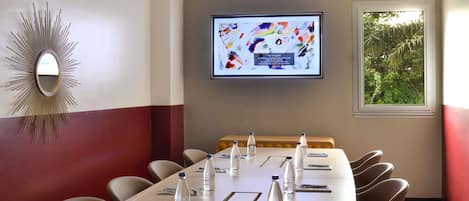Un salón de conferencias con una mesa larga, sillas, botellas de agua y una pantalla de televisión que muestra una imagen.
