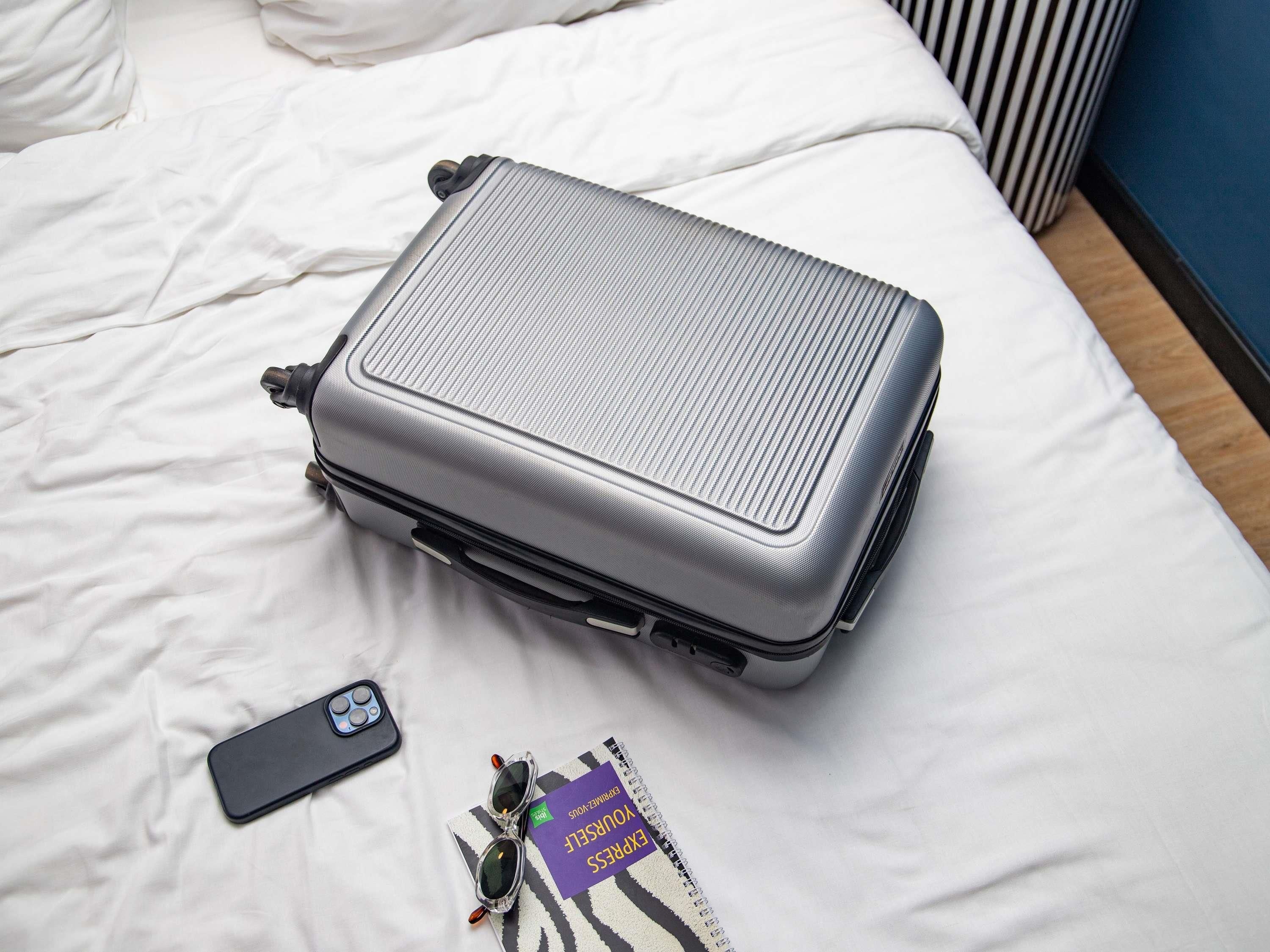 Een zilveren koffer op een bed, met een smartphone en een boek in de buurt.