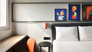 A hotel room with a bed, a desk, an orange chair, a small table, and three artworks on the wall. - ibis Styles Abidjan Plateau (Abidjan)
