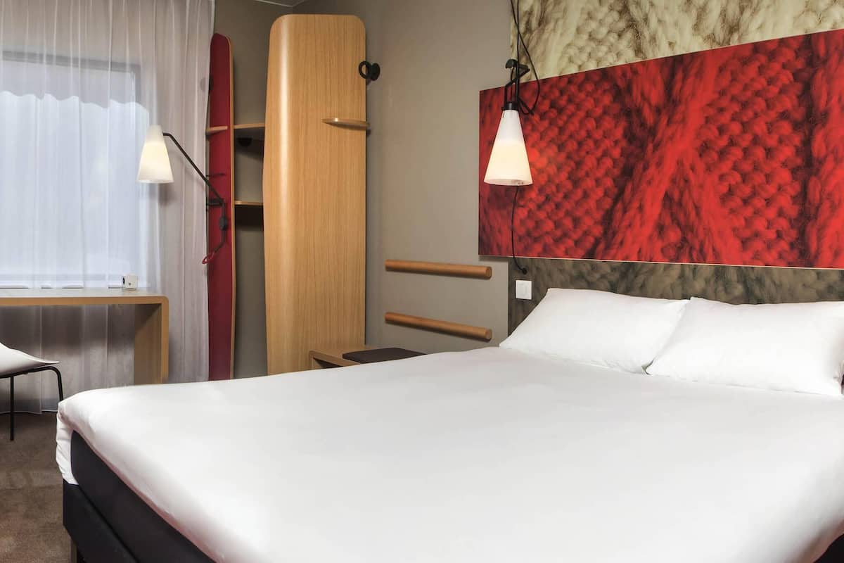 A modern hotel room with a large bed, a desk, and a chair.