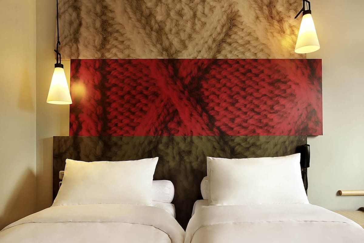 A hotel room with a large bed, two bedside lamps, and a textured wall above the bed.