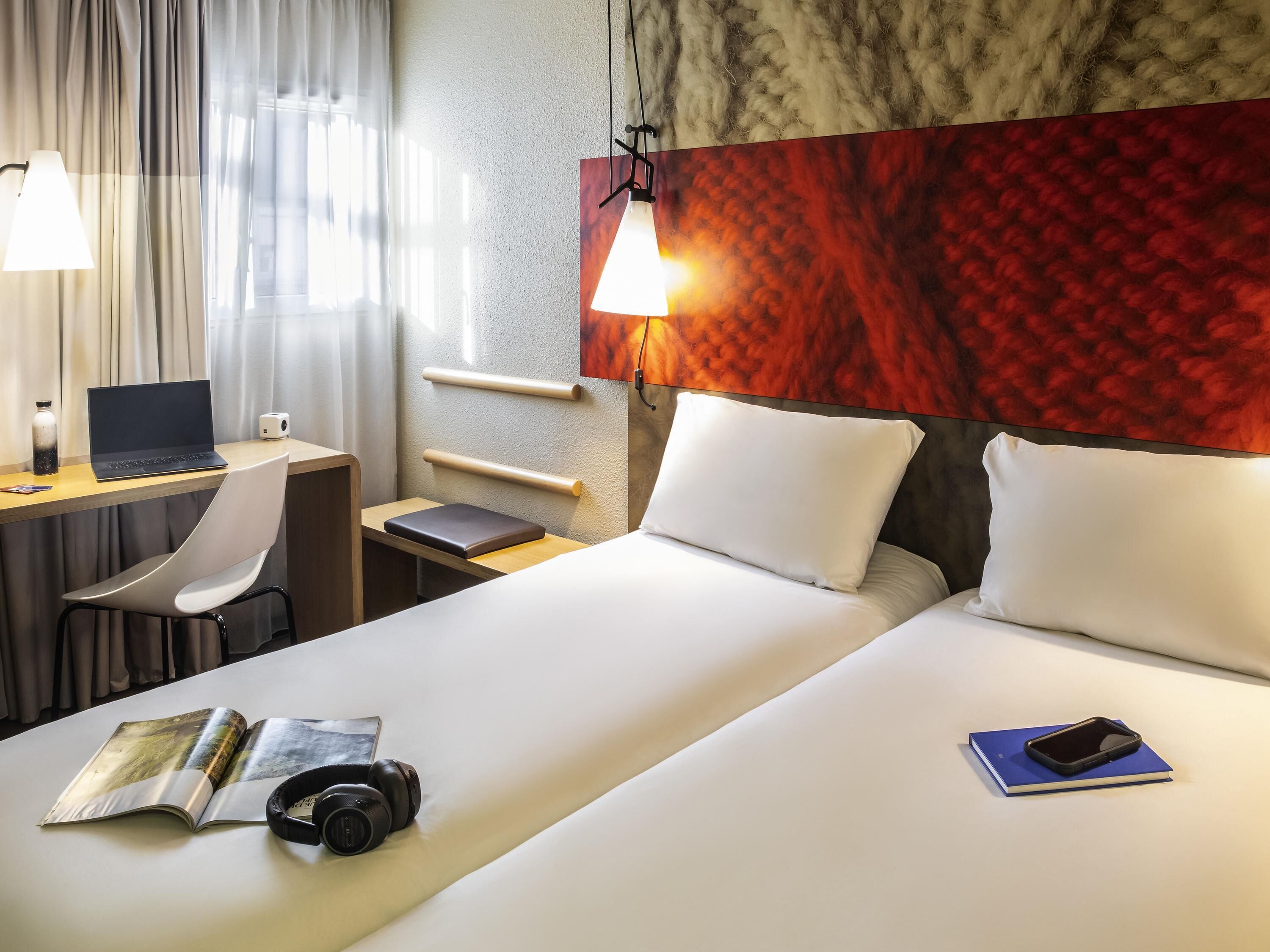 A hotel room with a bed, desk, chair, laptop, and a magazine.