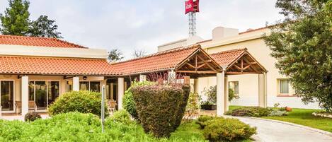 Un hotel con techo de tejas rojas, mobiliario exterior cubierto y una bandera en una torre.