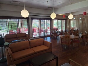 A spacious indoor area with multiple seating arrangements, including sofas and tables, and large windows with blinds. - ibis Setubal (Setubal)