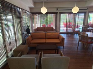 Una sala de estar moderna con un sofá, sillas, una mesa de centro y ventanas grandes con persianas.