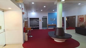 A hotel lobby with a red carpet, a central column, a reception desk, and a staircase.