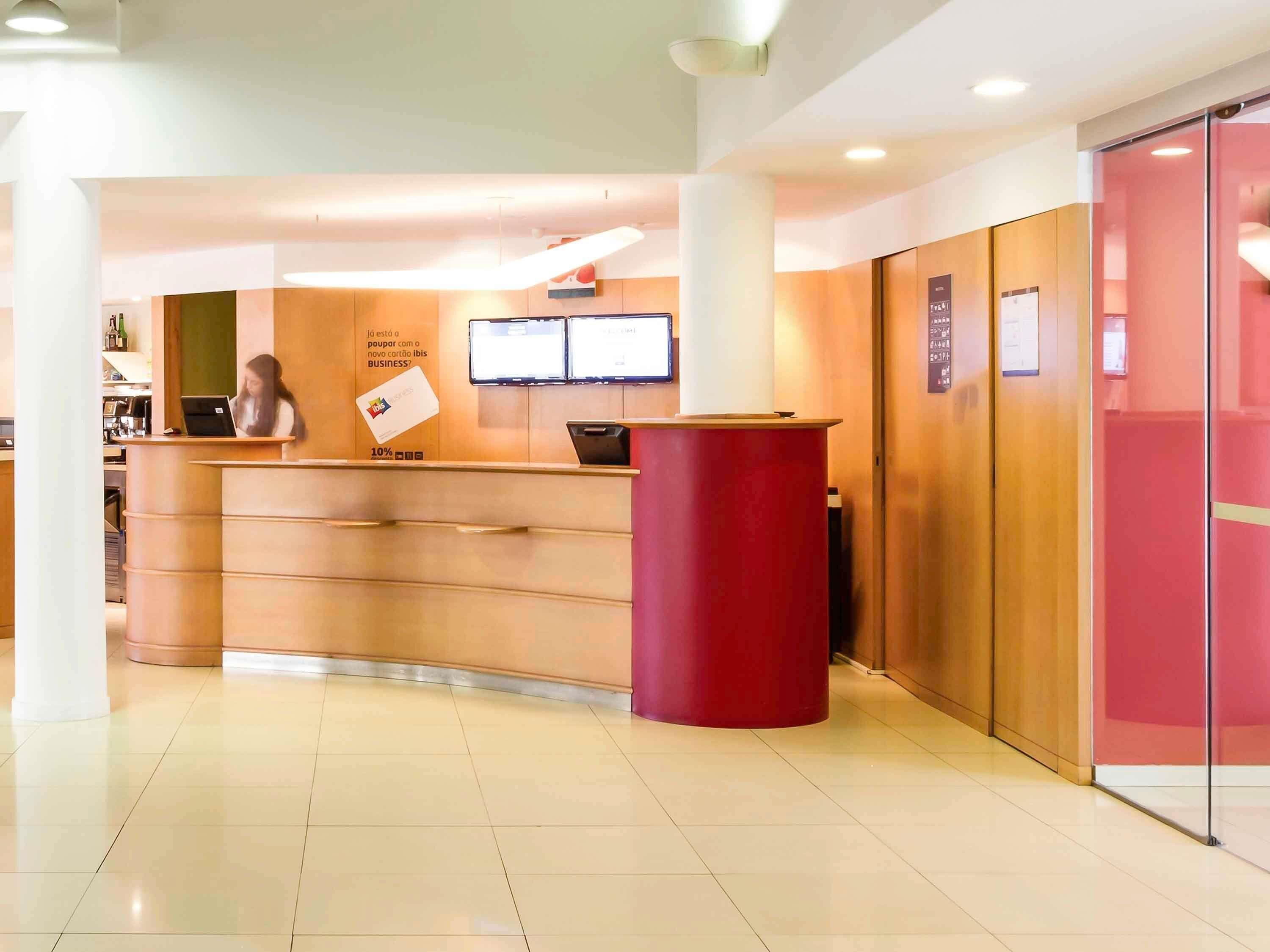 A reception desk with a laptop, a digital screen, and a red pillar.