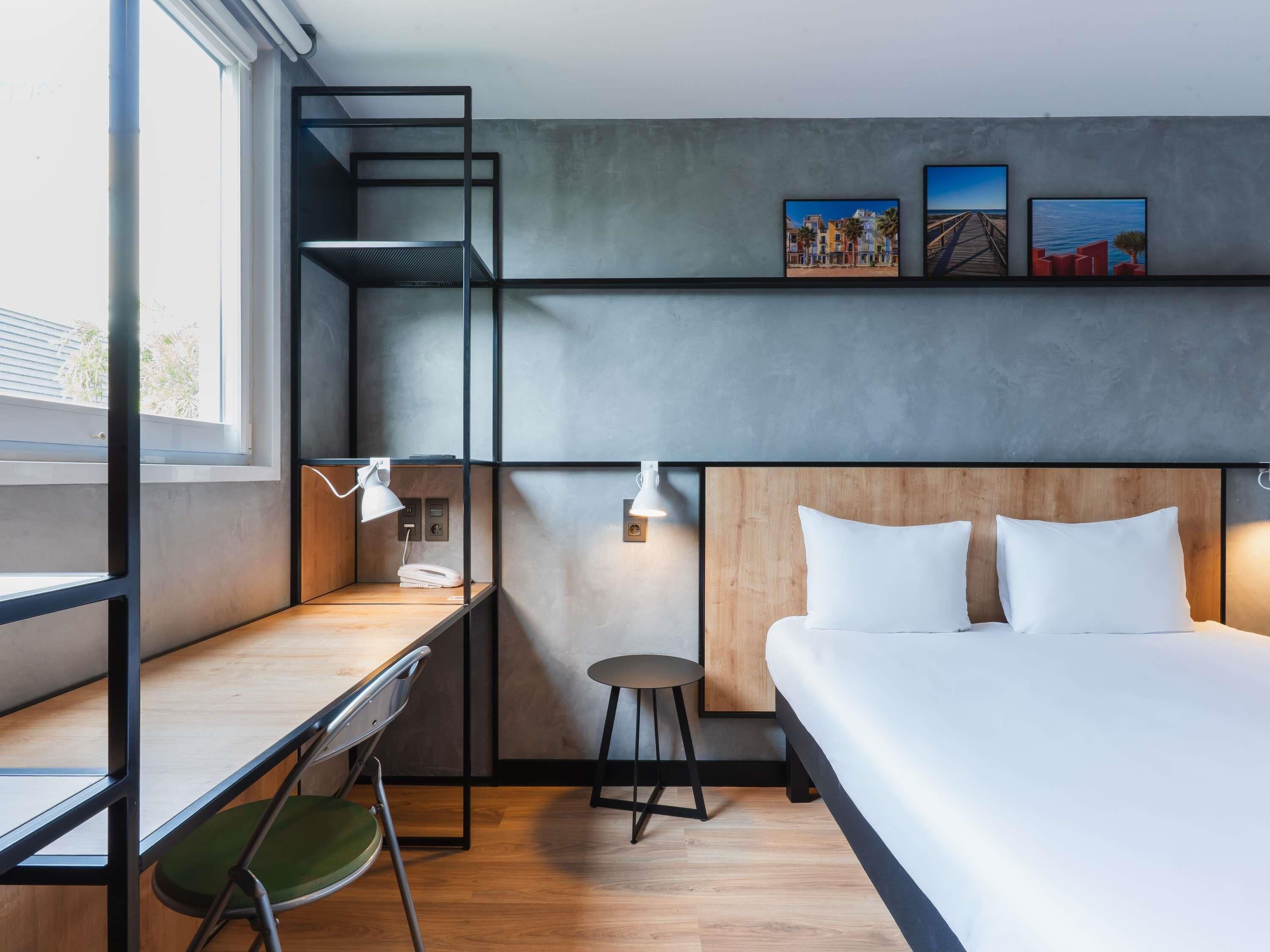 Una habitación de hotel moderna con escritorio, silla, cama y una obra de arte en la pared.