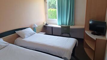 A hotel room with two beds, a desk with a chair, a television, and a window with curtains.