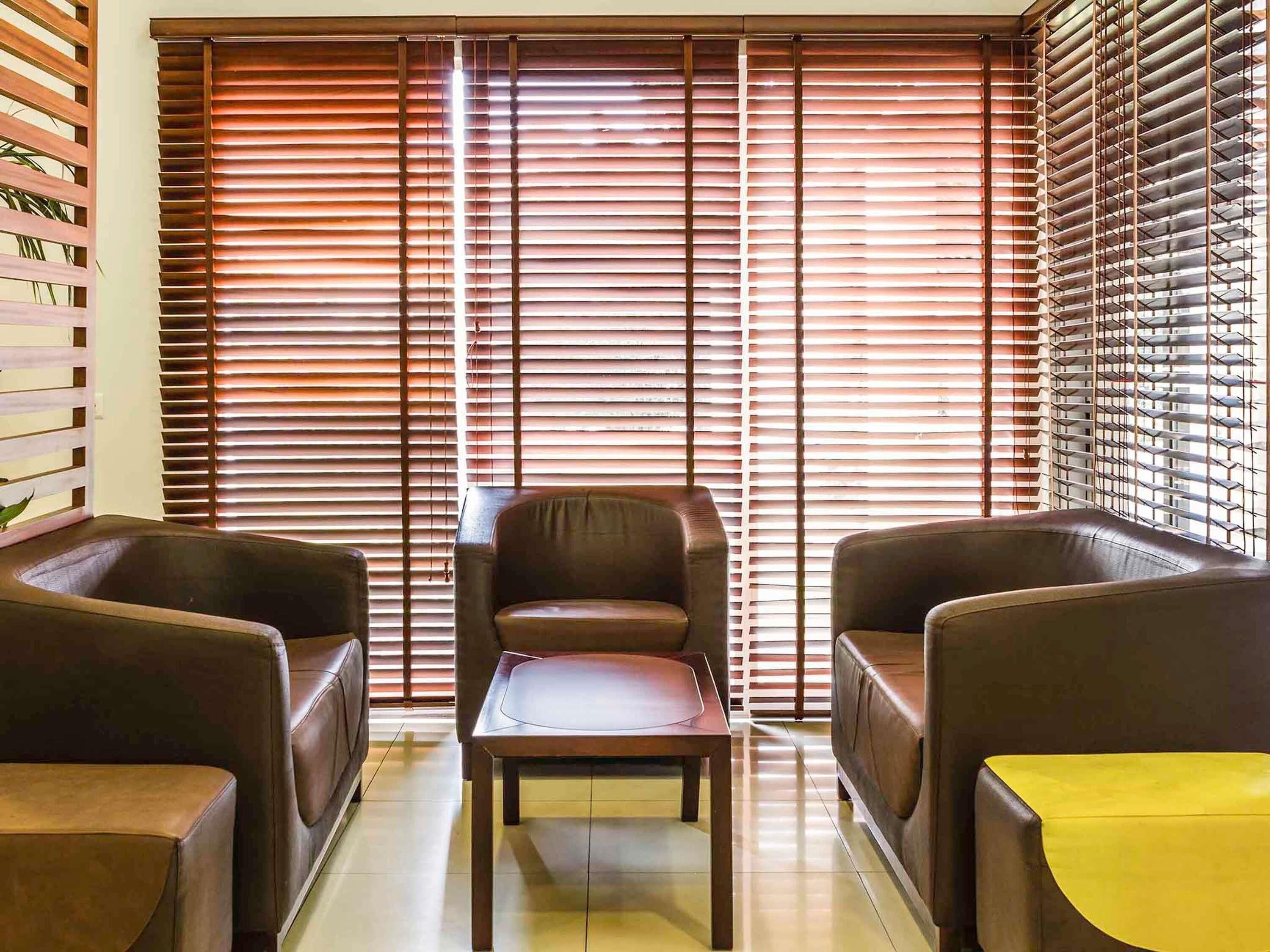 Una habitación con un gran ventanal con persianas horizontales, un sillón de cuero marrón, una mesa de madera y un mantel amarillo.