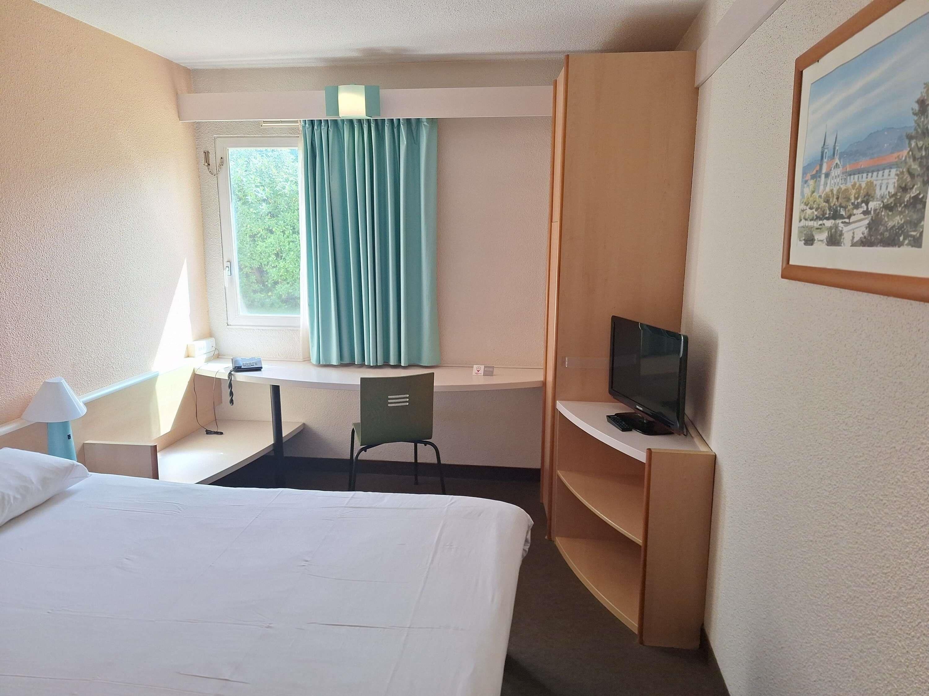 Una habitación de hotel con cama, escritorio, silla, televisión y un cuadro en la pared.