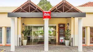 A hotel entrance with a sign for ibis hotels, a glass door, and potted plants. - ibis Setubal (Setubal)