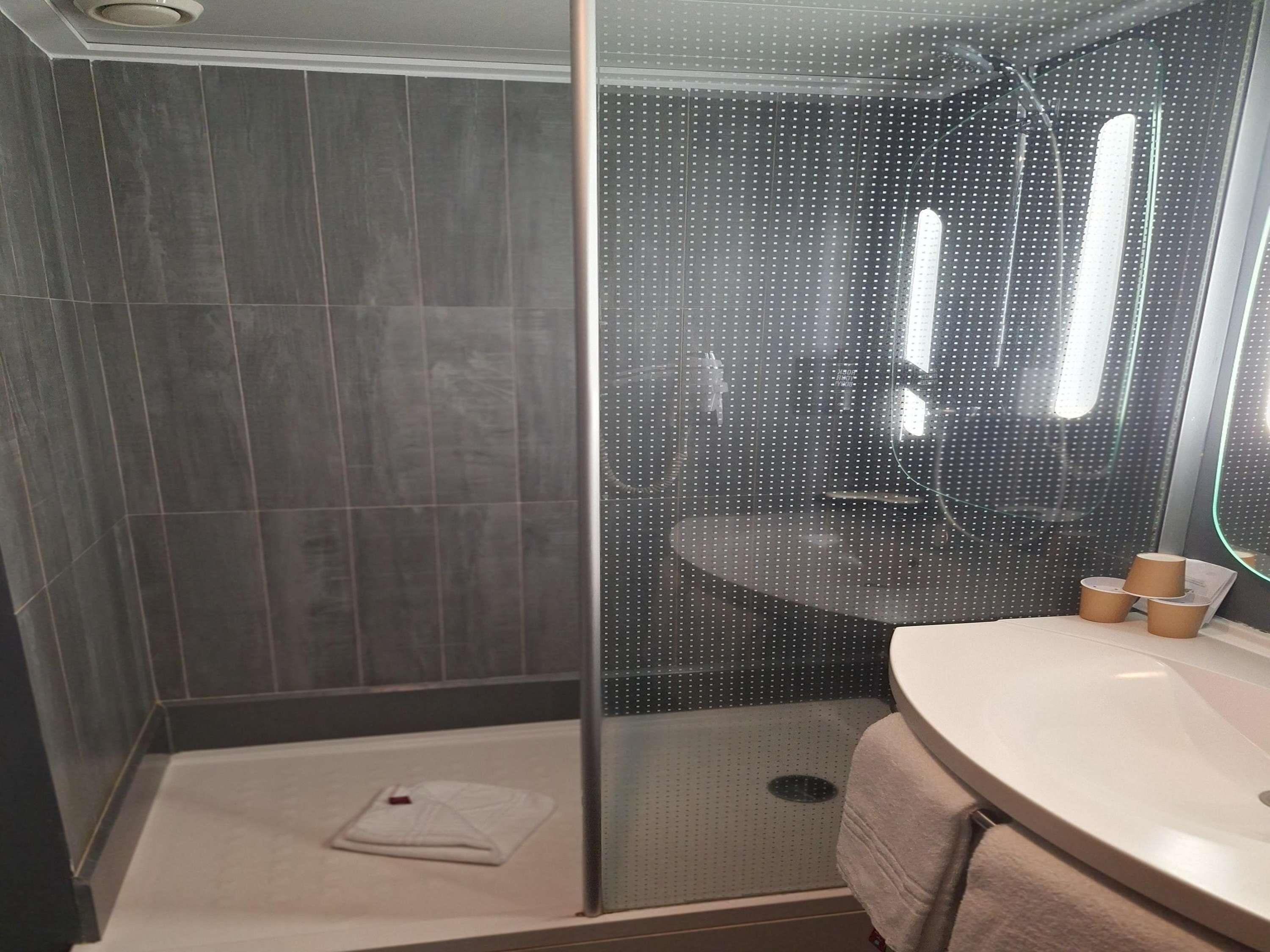 Un baño moderno con cabina de ducha de vidrio, un lavabo blanco y un perchero para toallas.